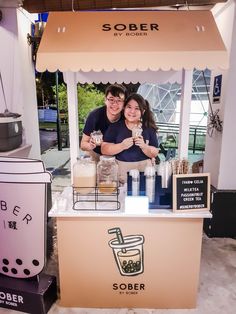 a man and woman standing behind a counter with drinks in front of them on display