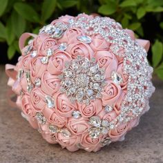 a bridal bouquet made with pink roses and crystal stones on the bottom, sitting on a stone surface