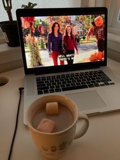 a laptop computer sitting on top of a desk next to a cup of hot chocolate