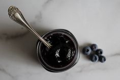 blueberries sit next to a jar of jam on a marble counter top with a spoon