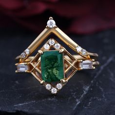 an emerald and diamond ring sitting on top of a black surface