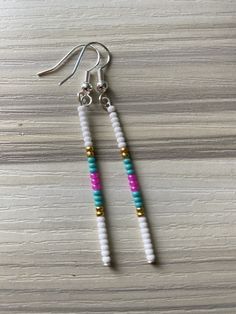 two white and pink beads are hanging from silver earwires on a wooden surface