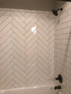 a white bathroom with herringbone tile and black faucet shower head in the corner