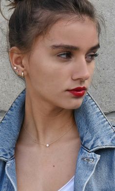 a woman with red lipstick wearing a denim jacket and white tank top is looking off to the side