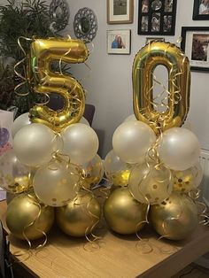 gold and white balloons in the shape of numbers are on a table with other decorations