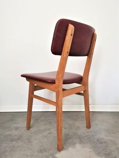 a wooden chair with brown leather seat and backrests on concrete floor next to white wall