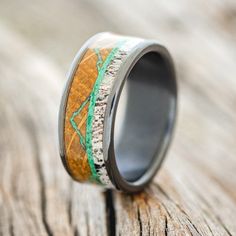 a wedding ring with wood and green inlays on the inside is sitting on a piece of wood