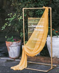 a yellow cloth draped over a sign on a stand in front of some potted plants