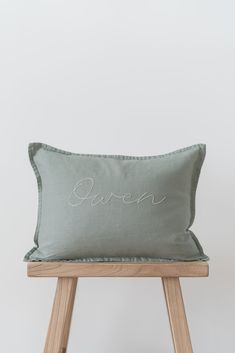 a green pillow with the word queen embroidered on it sitting on a wooden stool in front of a white wall