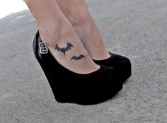 a woman's foot with a bat tattoo on her left leg and black shoes