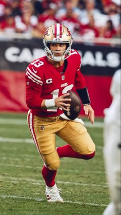 a football player holding a ball on top of a field with people in the background