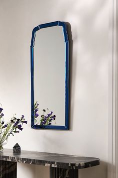 a blue mirror sitting on top of a table next to a vase filled with flowers