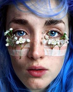 a woman with blue hair and flowers on her face is looking at the camera while she has