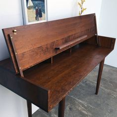 a wooden desk with an open drawer on it's left side and a painting on the wall behind it