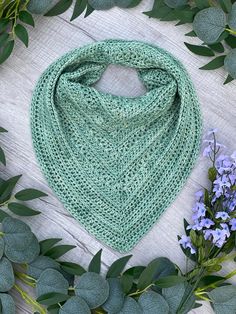 a green knitted scarf sitting on top of a wooden table next to blue flowers