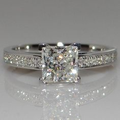 an engagement ring with a princess cut diamond in the center and side stones on each band