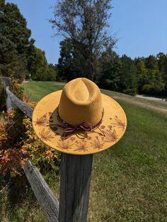 This tumeric yellow hand burnt wide brim fedora would make a perfect addition to any nature lover's wardrobe. The faux suede earthen yellow material burns a rich brown allowing the design to stand out. On the backside brim of the hat I hand burnt and shaded dandelion plants. On the front of the crown I burnt a single dandelion plant. I distressed the hat with stitch marks along the crown and brim of the hat. The design is original and completely free-handed. For a finishing touch I added a brown Yellow Bohemian Fedora Straw Hat, Yellow Bohemian Straw Hat With Curved Brim, Bohemian Yellow Straw Hat With Short Brim, Yellow Bohemian Straw Hat With Short Brim, Handmade Yellow Wide Brim Straw Hat, Yellow Bohemian Wide Brim Straw Hat, Yellow Curved Brim Fedora For Kentucky Derby, Spring Festival Hat With Flat Crown, Yellow Fedora Sun Hat For Kentucky Derby