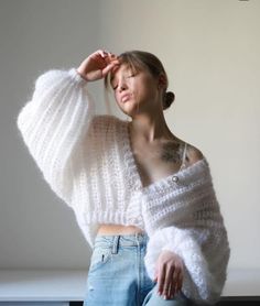 a woman wearing a white sweater and jeans poses for the camera with her hands on her head