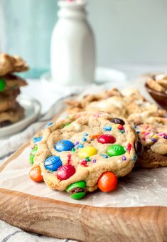 a cookie with m & m cookies on it sitting on a cutting board next to other cookies