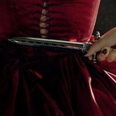 a woman in a red dress is holding a knife with her hand on the belt