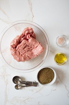 ingredients to make meat in bowls on a white counter top with spoons and seasonings