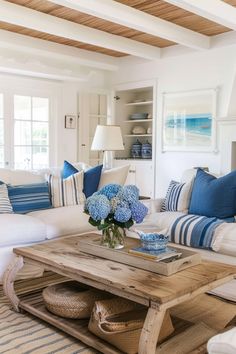 a living room filled with white furniture and blue pillows on top of it's couches