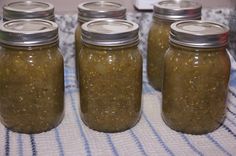 four jars filled with pickles sitting on top of a blue and white table cloth