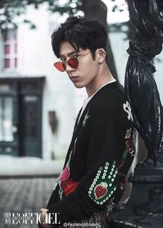 a young man wearing red sunglasses leaning on a black pole in front of a white building