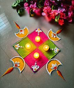 a decorated diya with lit candles on the floor next to some pink and yellow flowers