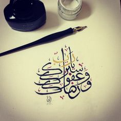 an arabic calligraphy is displayed on a table with some ink and a brush next to it