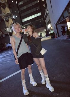 two young women standing in the middle of an empty street at night, one drinking orange juice