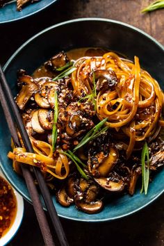 a bowl filled with noodles and mushrooms on top of a wooden table next to chopsticks