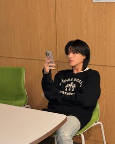 a woman sitting at a table with a cell phone in her hand and wearing a black sweatshirt