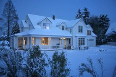 a white house is covered in snow at night with lights on the windows and porch