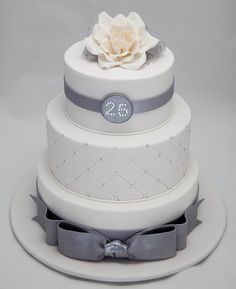 a three tiered wedding cake with a white flower on top and grey ribbon around the bottom