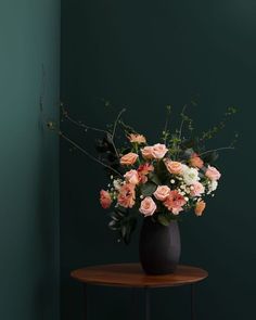 a black vase filled with pink and white flowers on top of a small wooden table