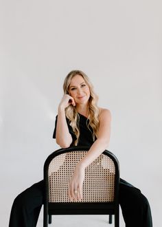 a woman sitting in a chair with her hand on her chin and looking at the camera