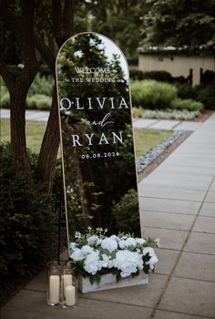 a wedding sign with flowers and candles on the side walk in front of a tree