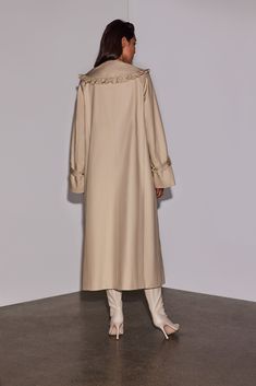 A romantic take on a utilitarian trench coat, an exaggerated collar trimmed in pleated ruffle is contrasted against wide sleeves, uninterrupted clean lines and a longer length. Featuring a concealed button placket finished with Italian recycled buttons a hidden frilled cuff adds an unexpected element allowing for multiple styling options. Elegant Oversized Gabardine Outerwear, Elegant Spring Outerwear With Fold Down Collar, Fall Daywear Outerwear With Ruffles, Fall Ruffled Outerwear For Daywear, Elegant Collared Outerwear With Covered Buttons, Elegant Cream Outerwear With Ruffles, Elegant Outerwear With Button Cuffs For Daywear, Chic Cream Outerwear With Ruffles, Chic Beige Outerwear With Ruffles