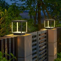 two modern outdoor lighting fixtures on top of concrete blocks in front of trees and bushes