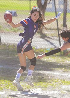 two girls playing football on a field with one holding the ball and another reaching for it