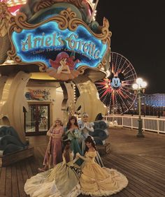 there are many statues on the deck of this amusement park at night with lights in the background