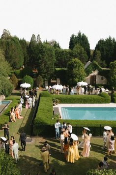 a group of people standing around a lush green field next to a swimming pool on top of a lush green hillside