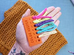 a person's hand holding an orange piece of string with colorful beads on it