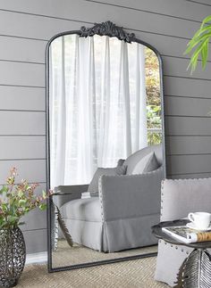 a large mirror sitting on top of a floor next to a couch and table in front of a window