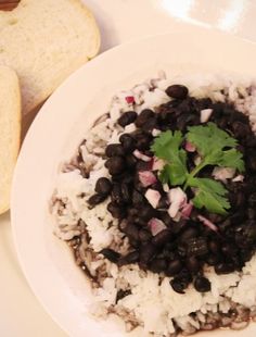 a white plate topped with rice and black beans next to a slice of bread on top of a table