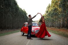 a man and woman dancing in front of an old red car on the side of the road