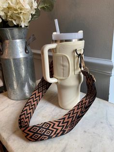 a white cup with a brown and black pattern on it next to a flower vase