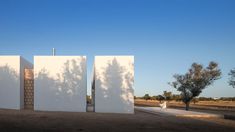 three large white structures sitting in the middle of a dirt field next to a tree