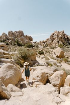 a woman wearing a straw hat walking on rocks in the desert with large boulders behind her